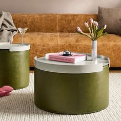 two tables with flowers and books on them in front of a brown leather couch,