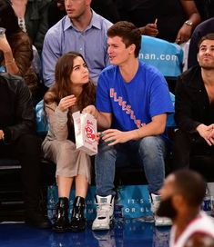 two people sitting next to each other in front of a crowd at a basketball game