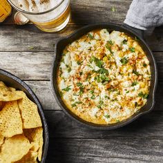 a pan filled with cheese and chips next to a glass of beer on top of a wooden table