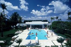 an outdoor swimming pool surrounded by palm trees and people in bathing suits on lounge chairs