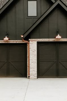 two garage doors are open in front of a brick wall and black house with brown shingles