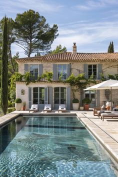 an outdoor swimming pool with chaise lounge chairs and umbrellas in front of a house