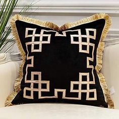 a black and gold pillow sitting on top of a white chair next to a potted plant