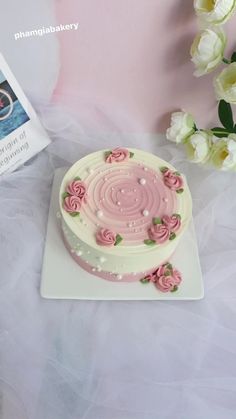 a cake with pink frosting and roses on it sitting on a table next to flowers