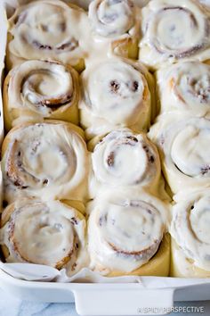 a white dish filled with cinnamon rolls covered in icing and sitting on a table