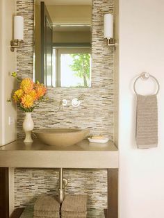 a bathroom sink sitting under a mirror next to a towel dispenser with flowers in it