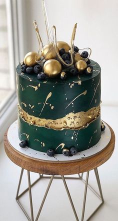 a green and gold decorated cake sitting on top of a wooden table next to a window