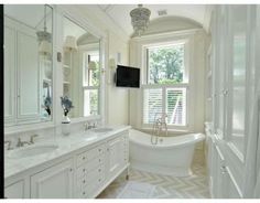 a white bathroom with a tub, sink and television on the wall in it's corner