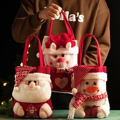 three small stuffed animals in santa's hats and holding shopping bags on a table