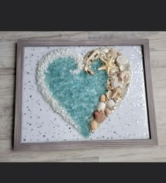 a heart made out of sea glass and shells on a white tray with a wooden frame