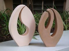 two large vases sitting on top of a white table next to some grass and bushes