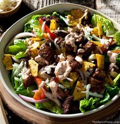 a salad with meat and vegetables in a bowl on a wooden table next to rice