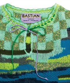 a green sweater with blue, yellow and black stripes on the bottom that says bastian