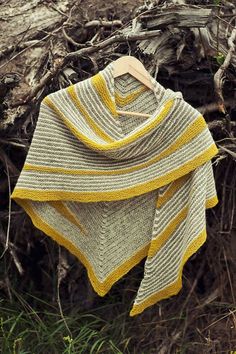 a yellow and white knitted shawl sitting on top of a pile of branches