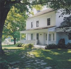 a white two story house sitting on top of a lush green field next to a tree