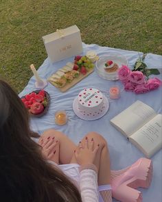 a woman sitting on top of a blue blanket next to a table filled with food