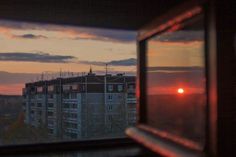 the sun is setting in front of some buildings as seen through a window at dusk