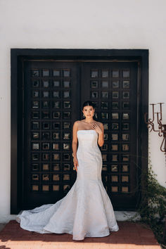 a woman standing in front of a black door wearing a white dress and holding her hand up to her face