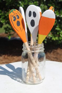 four wooden spoons with painted faces in a mason jar on a table outside,