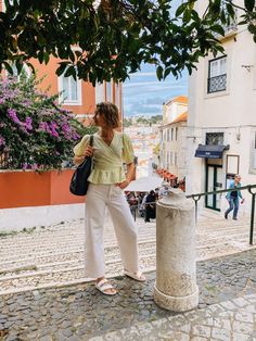 a woman standing next to a trash can on a cobblestone street with buildings in the background