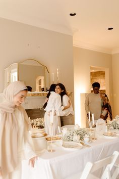 a group of people standing around a dining room table with white linens on it