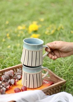 a person is holding a coffee mug over a tray with grapes and other items on it