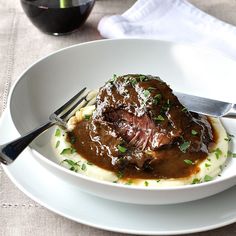 a white plate topped with meat and gravy next to a glass of wine