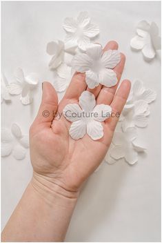 a person's hand holding three white flowers on top of paper petals in the shape of butterflies