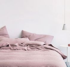 an unmade bed with pink linens and pillows in a white walled bedroom area