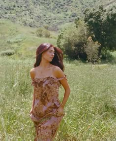 a woman is standing in the grass with her hands on her hips and looking off into the distance