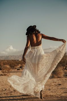 a woman in a white dress is walking through the desert with her back to the camera