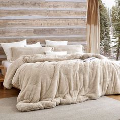 a large bed covered in white blankets and pillows next to a wooden wall with snow on it