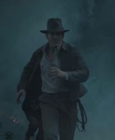 a man with a hat and coat walking in the fog while wearing a fedora