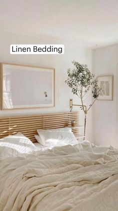 an unmade bed with white sheets and pillows in a small room next to a potted plant