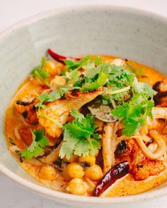 a white bowl filled with food and garnished with cilantro, red pepper, and green leafy greens