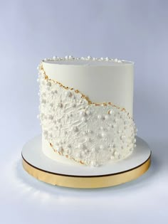 a white and gold wedding cake with pearls on the top is sitting on a plate