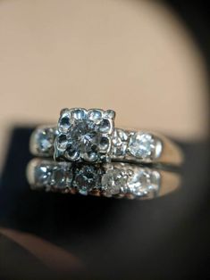 a close up view of a diamond ring on a black surface with a reflection in the background