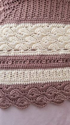 a crocheted blanket on top of a bed with pink and white stripes in the middle