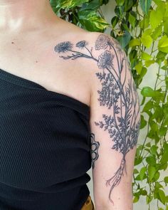 a woman with a flower tattoo on her left arm and shoulder is standing in front of a green plant