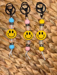 three key chains with smiley faces on them hanging from a woven piece of wood next to each other