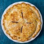 a baked pie on a white plate with blue table cloth and wooden utensils