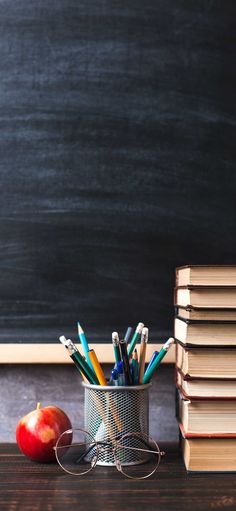 an apple, books and pencils on a desk in front of a blackboard