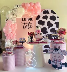 a table topped with cakes and balloons next to a cow theme sign that says elamio tete