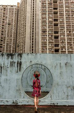 a woman in a dress and hat walking past tall buildings