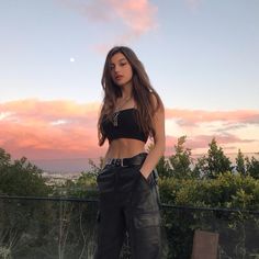 a woman standing on top of a wooden platform next to a lush green field at sunset