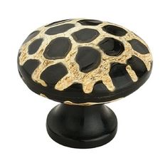 a black and gold cabinet knob with an animal print pattern on the top, in front of a white background