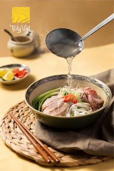 a person pouring soup into a bowl with chopsticks on the table next to it