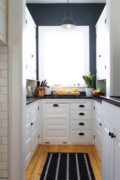 a narrow kitchen with white cabinets and black counter tops is seen from the doorway to the dining room