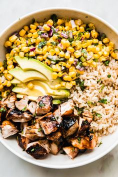 a bowl filled with chicken, rice and avocado on top of a table