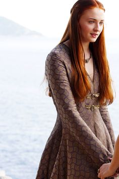 a woman with long red hair standing next to the ocean